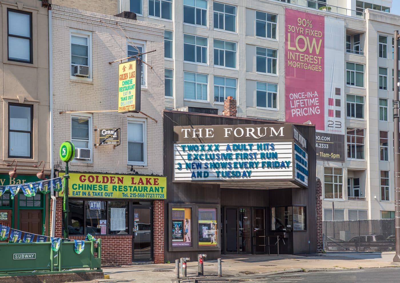 The Forum Theater at 2208 Market Street, Philadelphia, in June 2012. Its marquee reads TWO XXX ADULT HITS, EXCLUSIVE FIRST RUN, 3 NEW SHOWS EVERY FRIDAY AND TUESDAY, with a Chinese restaurant next door and a condominium tower behind advertising low interest mortgages.